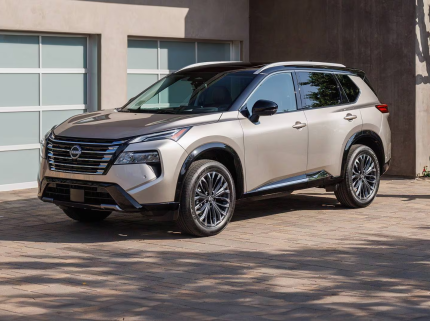 Angle view of the 2025 Nissan Rogue parked in front of a garage, showcasing its sleek crossover SUV design and bold V-Motion grille for car leasing enthusiasts.
